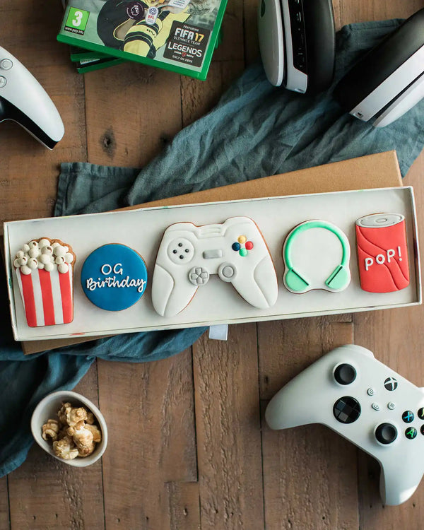 Honeywell Bakes Gamers Biscuit Gift Set - Gaming-themed cookies in a box with controllers and pop corn on a wooden surface