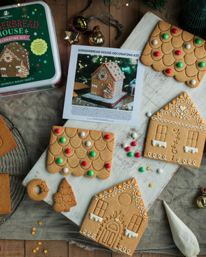 Honeywell Bakes Gingerbread House Decorating Kit,  gingerbread house pieces with a printed instruction sheet, a green tin box, and several decorated gingerbread house pieces