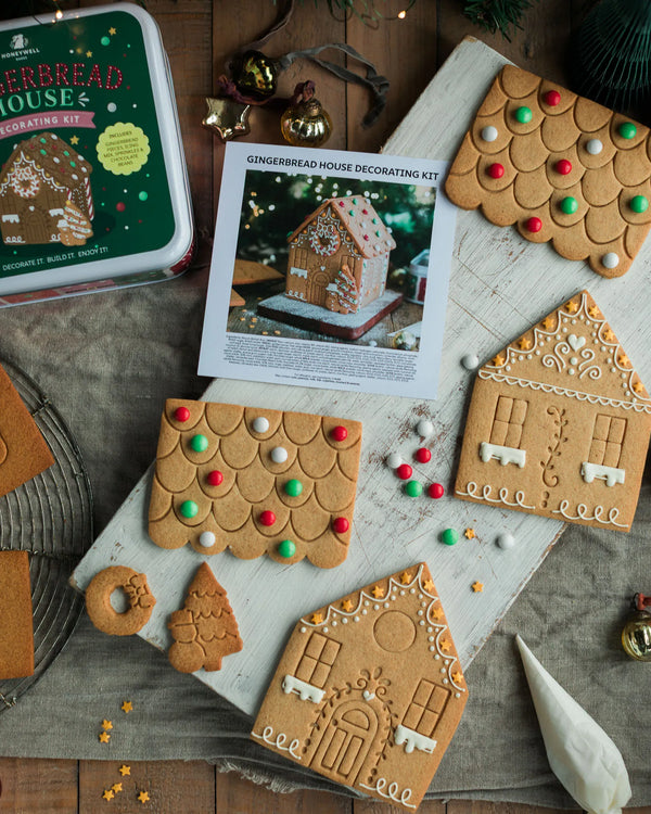 Honeywell Bakes Gingerbread House Decorating Kit,  gingerbread house pieces with a printed instruction sheet, a green tin box, and several decorated gingerbread house pieces