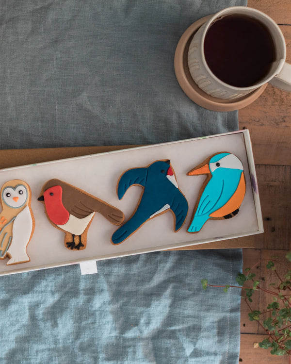 Honeywell Bakes Great British Birds Biscuit Gift - Box of bird-shaped cookies on a wooden table with a cup of coffee.
