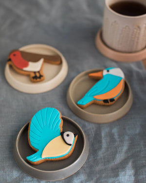 Honeywell Bakes Great British Birds Biscuit Gift - Three bird-shaped cookies on ceramic plates with a cup of tea in the background.