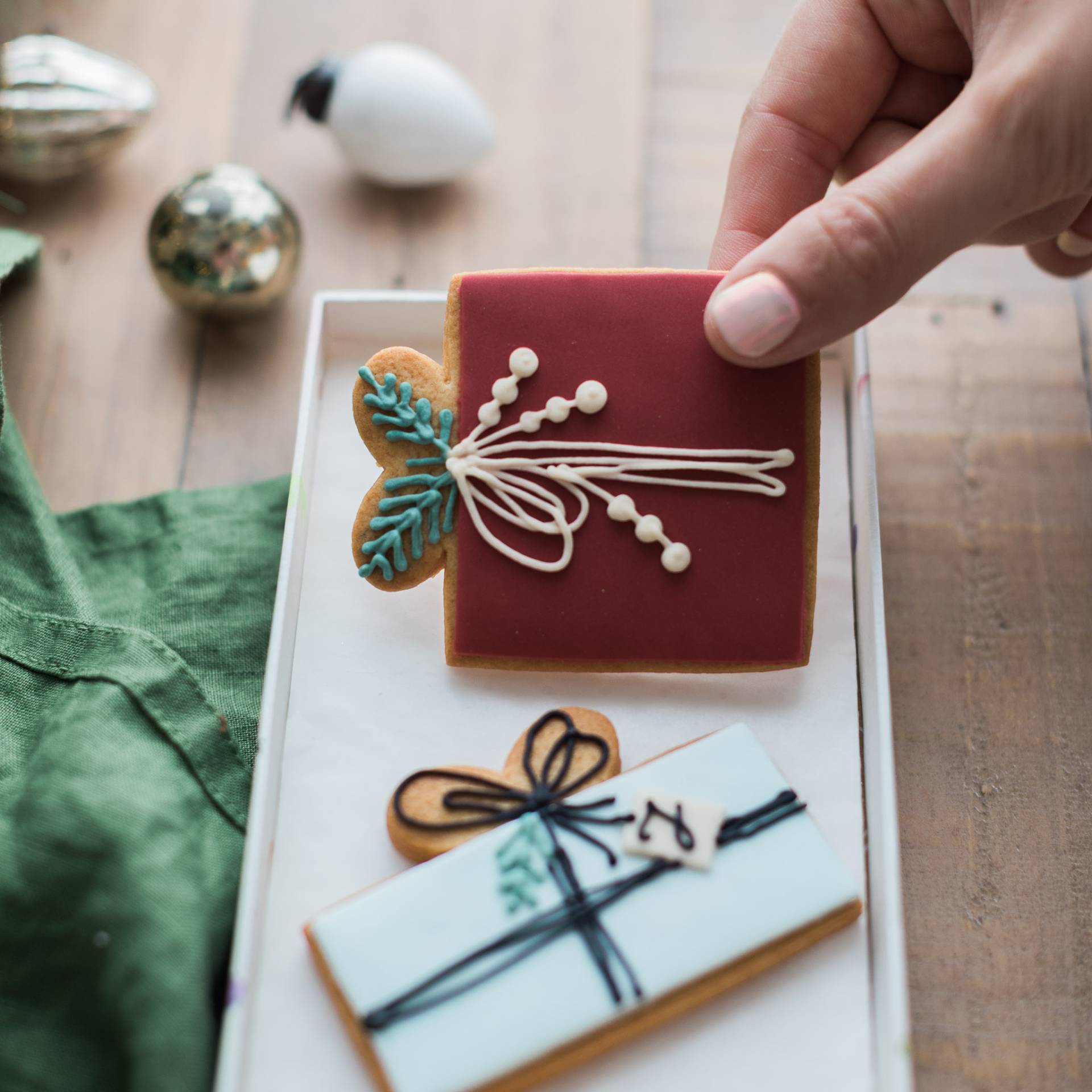 Decorative cookies with icing on a white tray, hand holding one cookie.