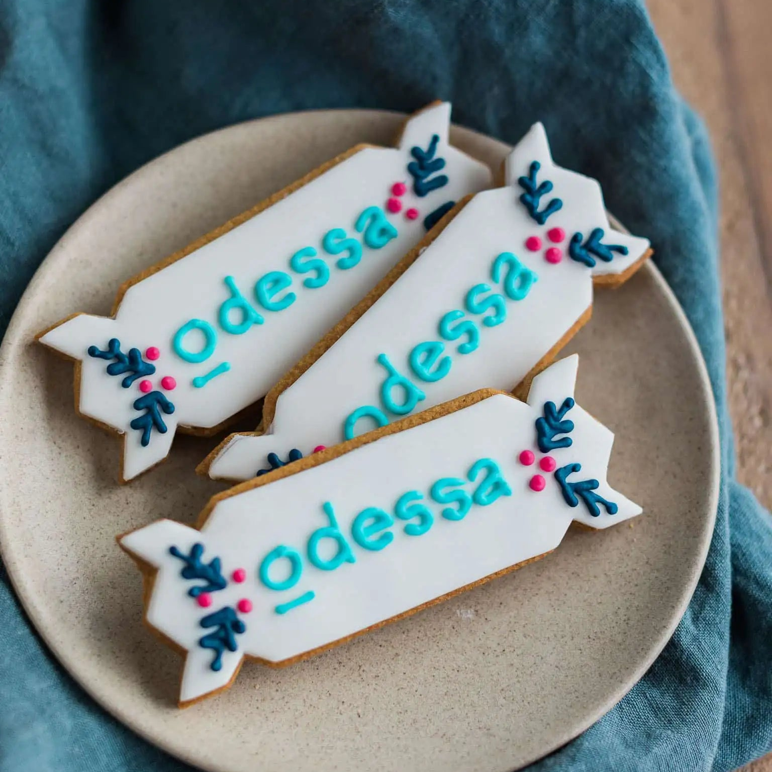 Decorative Christmas cracker shaped cookies with 'Odessa' logo hand iced in brand colours on a beige plate
