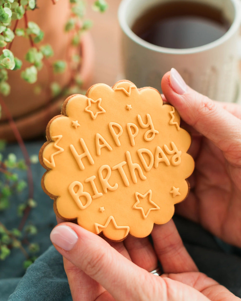 Honeywell Bakes Happy Birthday Biscuit - Hand holding a 'Happy Birthday' cookie with a cup of coffee in the background
