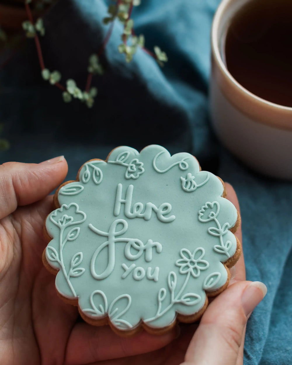 Honeywell Bakes Here For You Biscuit - Hand holding a decorative cookie with 'Here for you' text, blurred cup of tea in the background