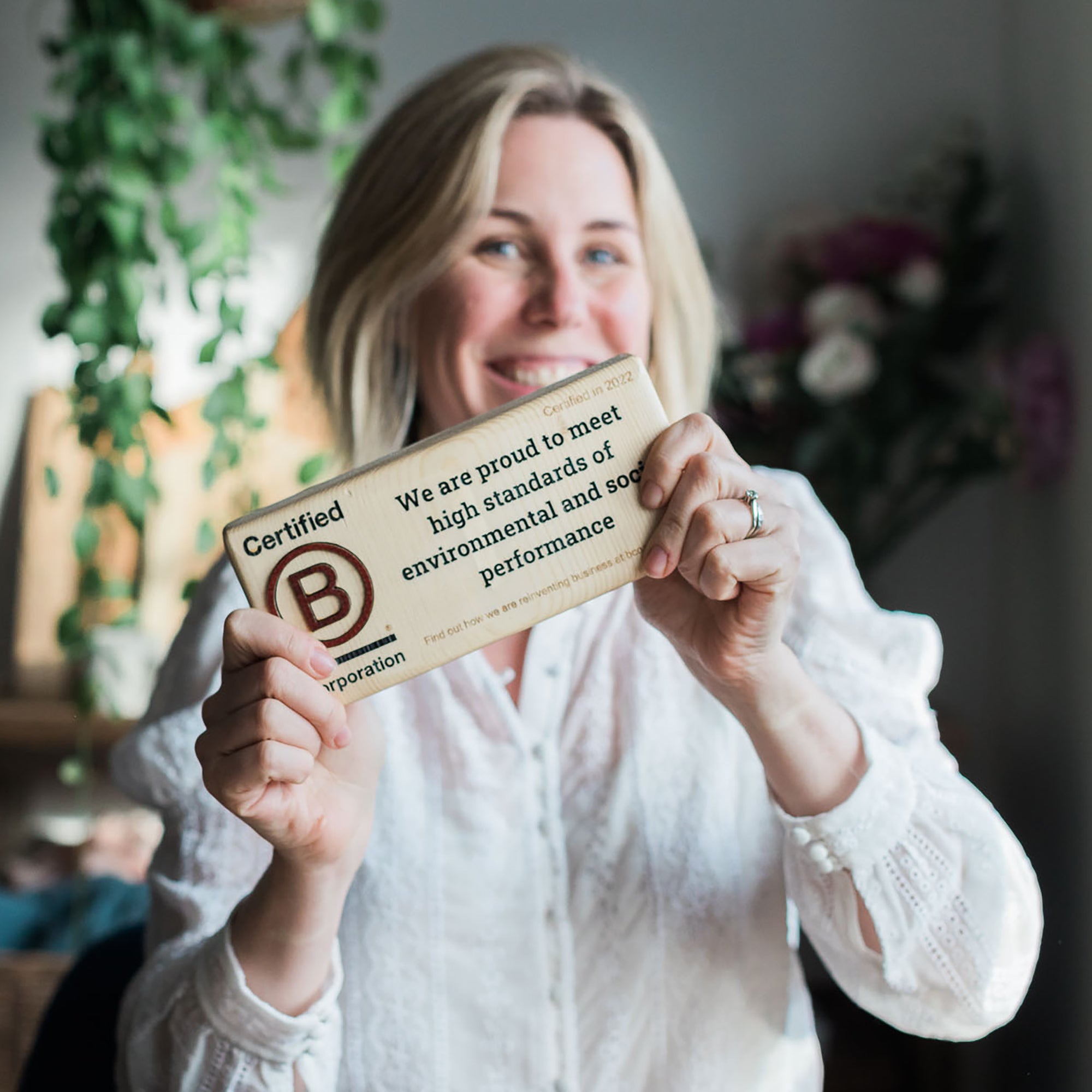 Honeywell Bakes founder Rebecca Honeywell holding a wooden sign with a B Corp certification logo and text.
