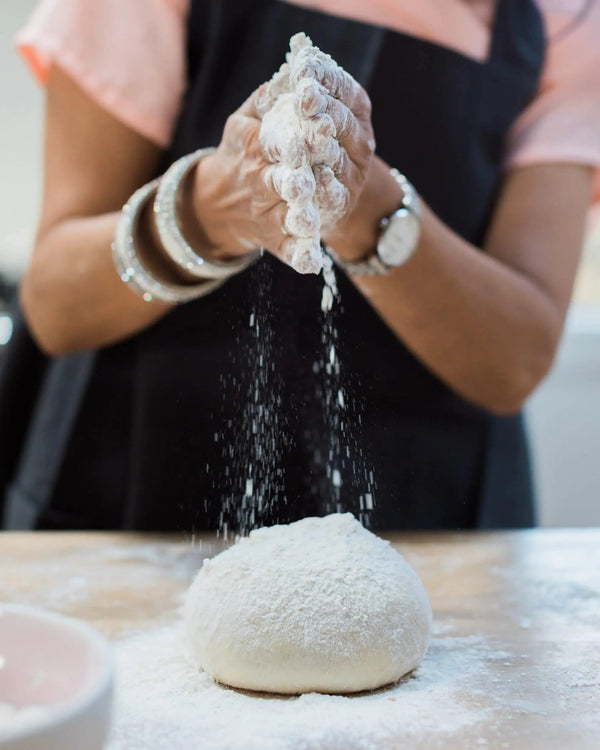 Honeywell Bakes Bread Bakers Subscription, Person sprinkling flour on a ball of dough on a wooden table.