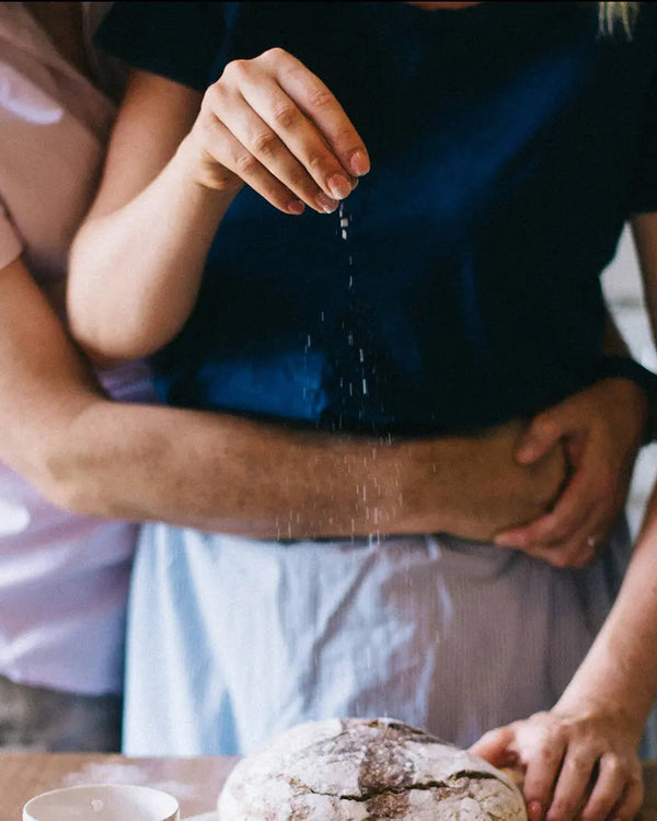 Honeywell Bakes Bread Bakers Subscription, Two people in a kitchen, one sprinkling flour on a loaf of bread.