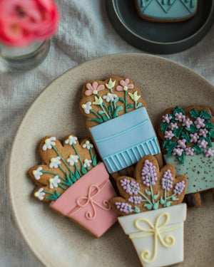 Honeywell Bakes House Plant Biscuit Gift Set - Decorative cookies shaped like potted plants on a plate with a floral arrangement in the background.