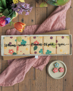 Honeywell Bakes If Mums Were Flowers Biscuit Gift Set - Box of cookies with floral designs and text on a wooden surface with flowers and a pink cloth.