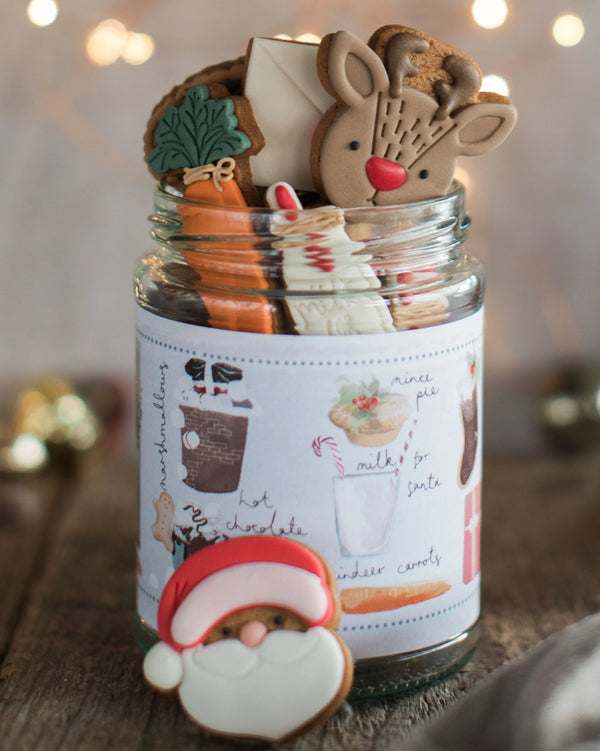 Honeywell Bakes Christmas Biscuits in a Jar -  A glass jar filled with assorted Christmas cookies, with a pretty hand illustrated label, designed as a Christmas Eve gift. Hand iced biscuits include a reindeer cookie, Santa, carrots for Rudolph and a glass of milk