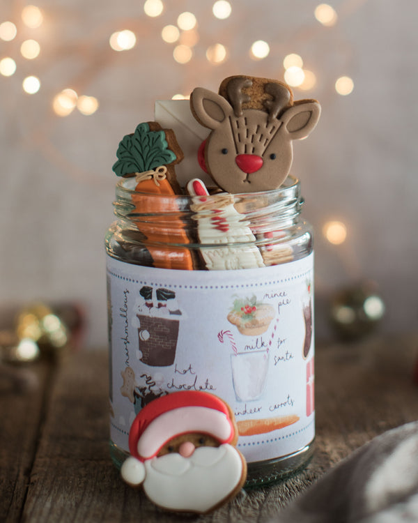 Honeywell Bakes Christmas Biscuits in a Jar -  A glass jar filled with assorted Christmas cookies, with a pretty hand illustrated label, designed as a Christmas Eve gift. Hand iced biscuits include a reindeer cookie, Santa, carrots for Rudolph and a glass of milk