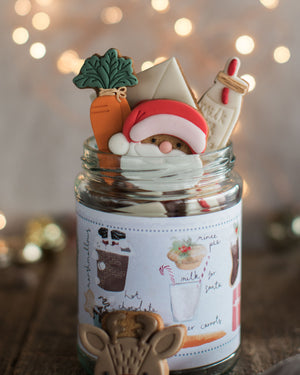 Honeywell Bakes Christmas Biscuits in a Jar -  A glass jar filled with assorted Christmas cookies, with a pretty hand illustrated label, designed as a Christmas Eve gift. Hand iced biscuits include a reindeer cookie, Santa, carrots for Rudolph and a glass of milk