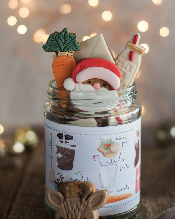 Honeywell Bakes Christmas Biscuits in a Jar -  A glass jar filled with assorted Christmas cookies, with a pretty hand illustrated label, designed as a Christmas Eve gift. Hand iced biscuits include a reindeer cookie, Santa, carrots for Rudolph and a glass of milk