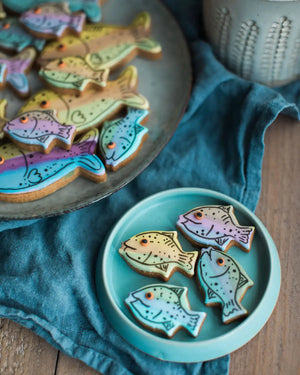 Honeywell Bakes Jar Of Fish - Fish-shaped cookies on a plate with a blue napkin and ceramic mug in the background.