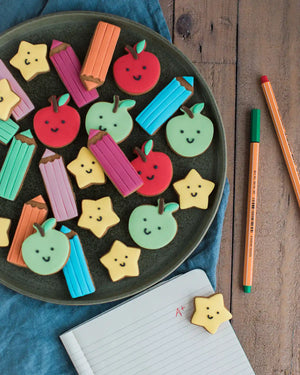 Honeywell Bakes Jar Of Smart Cookies - Decorative cookies shaped like apples, pencils, and stars on a plate with school supplies around.