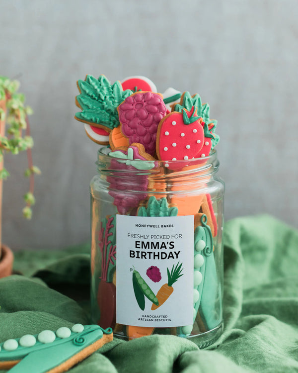 Honeywell Bakes Personalised Gardeners Fruit and Vegetable Biscuit Jar - Jar of colourful cookies with a 'Freshly Picked for Emma's Birthday' label on a green fabric background.