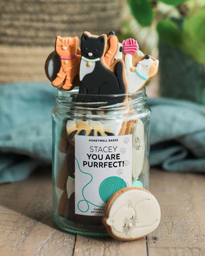 Personalised jar of cat-shaped biscuits from Honeywell Bakes, a cute gift for cat lovers with a custom label.
