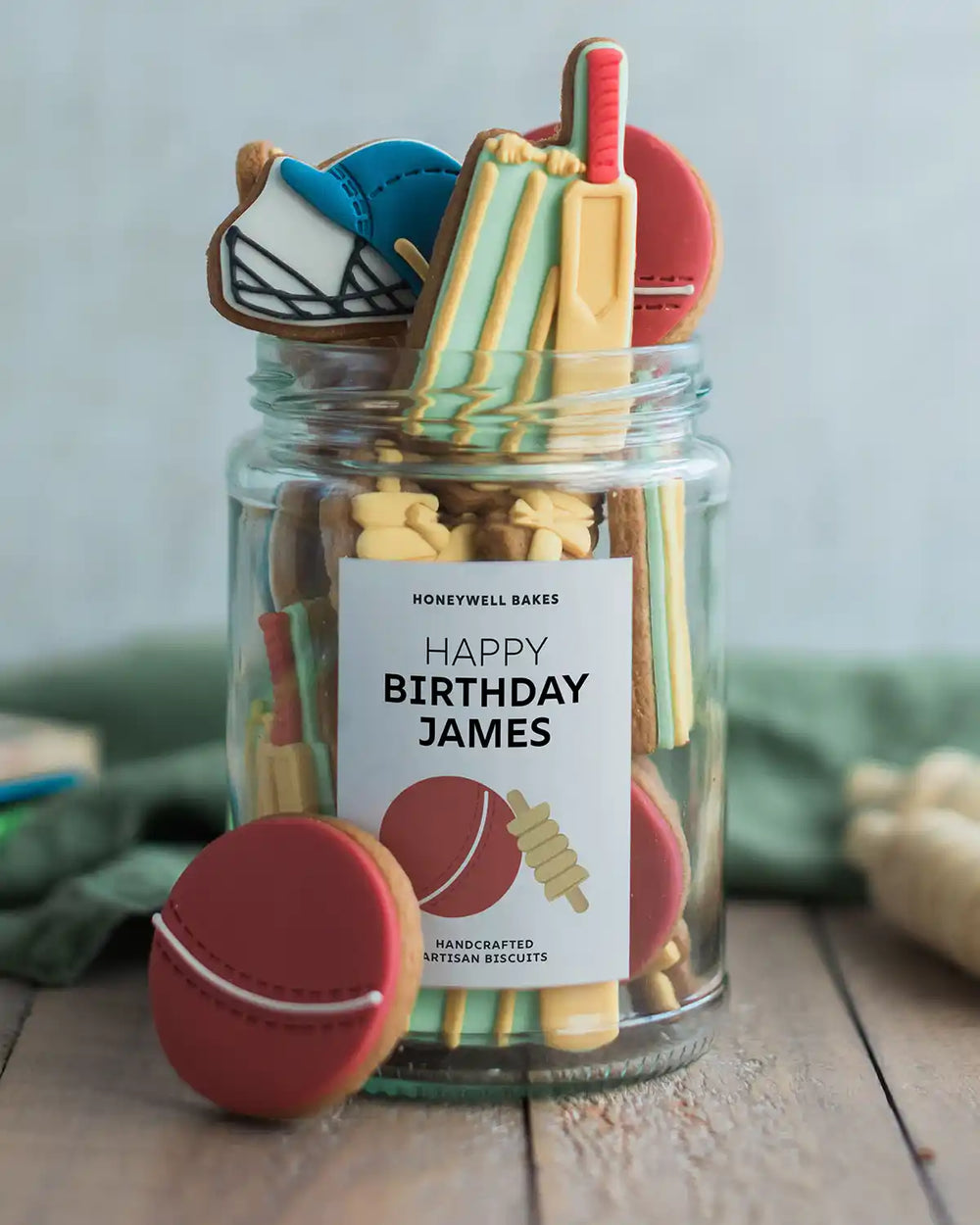 Honeywell Bakes Jar of Cricket Biscuit Gift - Jar of cookies with sports-themed shapes and a personalised label on a wooden surface.
