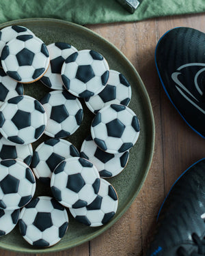 Honeywell Bakes Jar of Football Biscuits - Football-shaped cookies on a green plate with a wooden surface and sports bag in the background.
