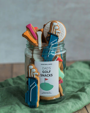 Honeywell Bakes Jar of Golf Biscuit Gift - Jar of cookie snacks shaped like golf clubs and balls with a label on a green cloth.
