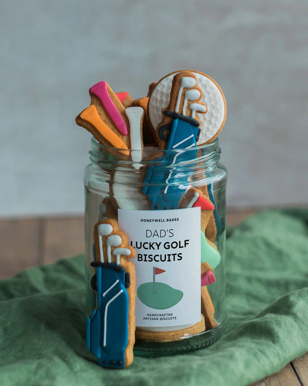 Honeywell Bakes Jar of Golf Biscuit Gift - Jar of 'Dad's Lucky Golf Biscuits' with cookie-shaped golf clubs and ball on a green surface.