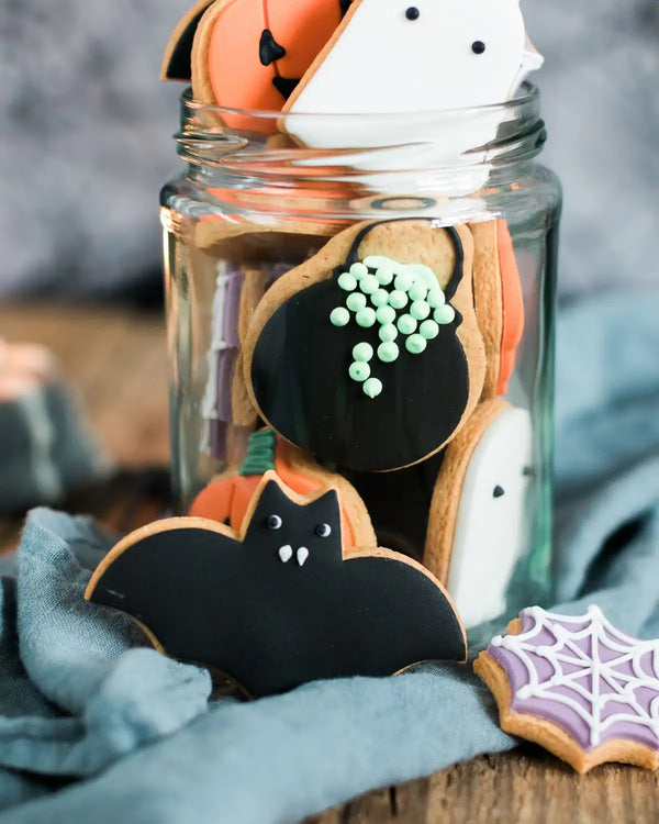 Honeywell Bakes Jar of Halloween Biscuits - Halloween-themed cookies in a glass jar on a wooden surface with a blue cloth.
