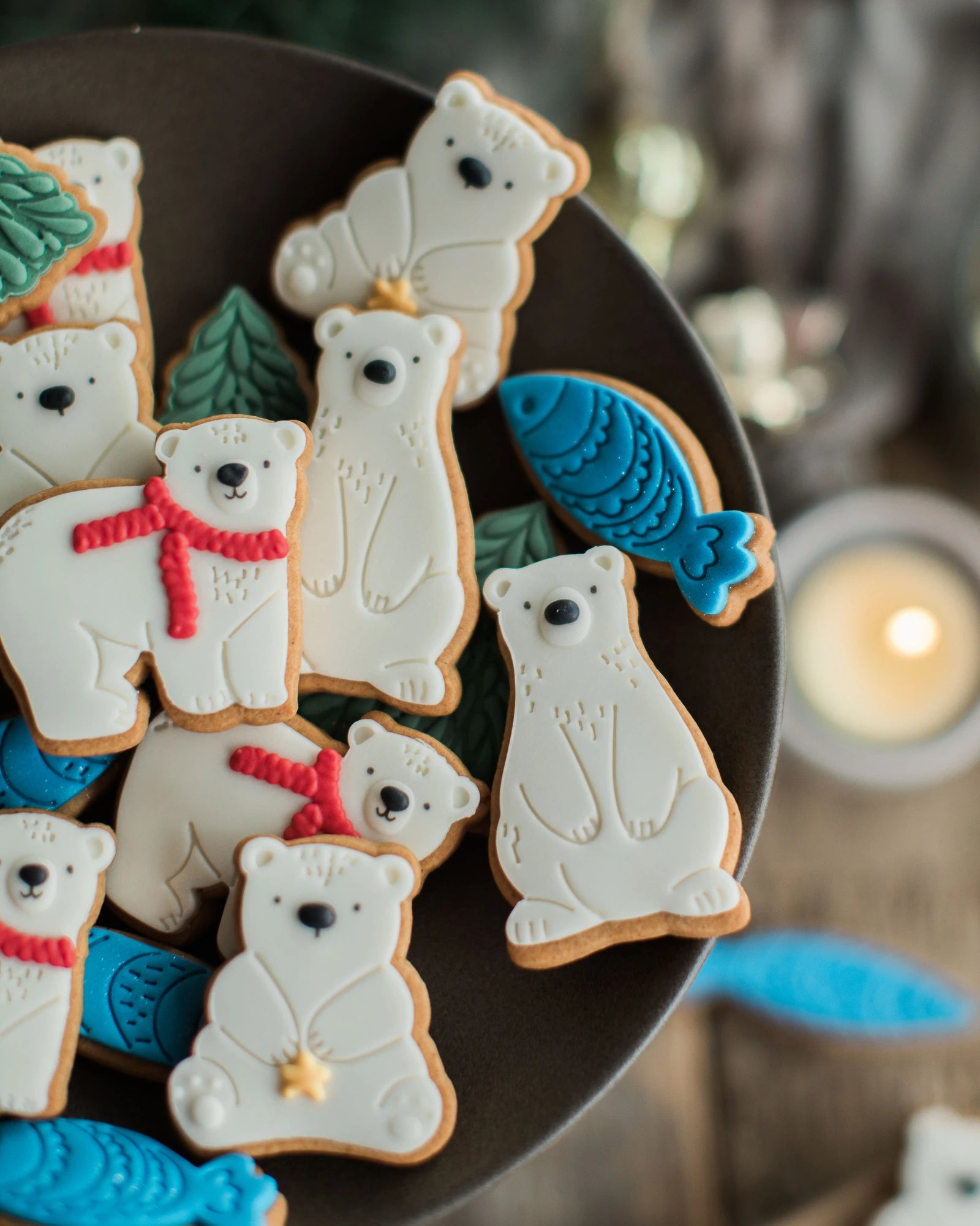 Honeywell Bakes Jar of Polar Bear Biscuits - Decorated polar bear and fish-shaped cookies arranged on a dark plate, with white icing on the bears, red scarves, blue fish, and small green tree accents on a rustic wooden surface.