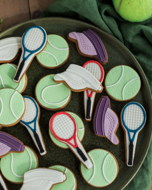 Honeywell Bakes Jar of Tennis Biscuit Gift - Cookies shaped like tennis rackets, balls, and shoes on a dark plate with a green cloth background.