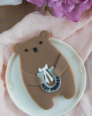 Honeywell Bakes Just Married Biscuit Bear - Cookie shaped like a bear with 'Just Married' inscription on a white plate with pink flowers in the background.