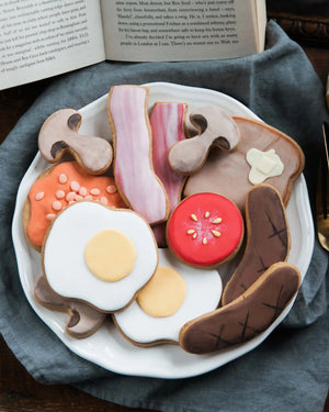 Honeywell Bakes Large Full English Biscuit Breakfast - Plate of cookie-shaped food items including eggs, bacon, and toast on a blue cloth with an open book in the background.