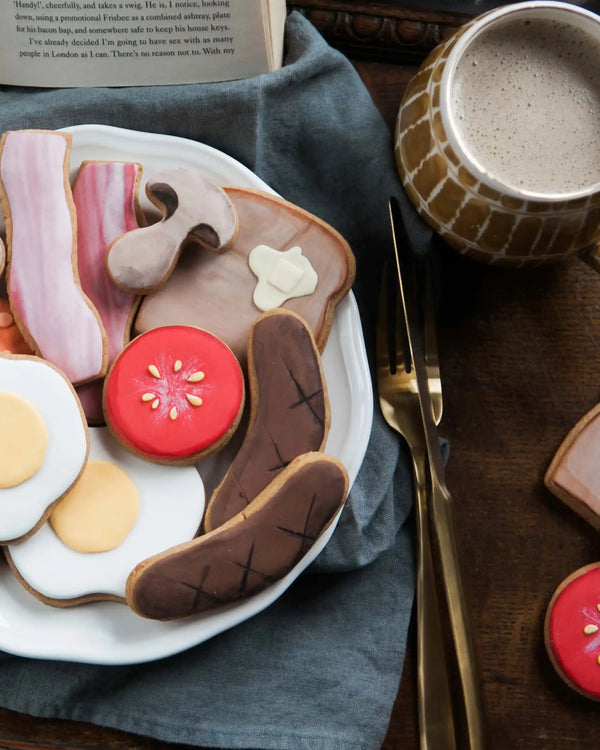 Honeywell Bakes Large Full English Biscuit Breakfast - Breakfast-themed cookies on a plate with a mug of coffee and cutlery on a wooden table.