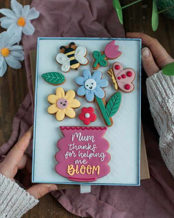 Honeywell Bakes Large Happy Biscuit Bloom Gift - Decorative biscuit set with floral and insect designs held by hands, featuring the text 'Mum thanks for helping me bloom'.