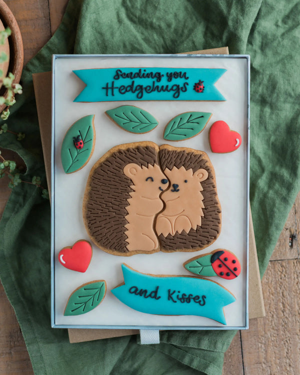 Honeywell Bakes Large Hedgehugs Biscuit Gift - Hedgehog biscuit design and text 'Sending you Hedgehugs and Kisses' on a green fabric background.