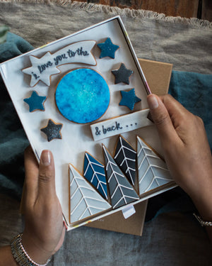 Honeywell Bakes Large I Love You To The Moon And Back Biscuit Gift Set - Box of decorated cookies with star and arrow designs held by a person.