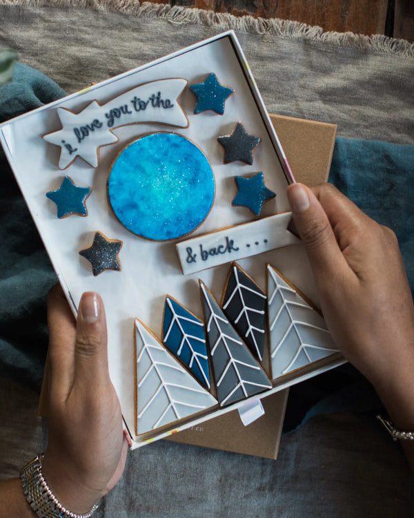 Honeywell Bakes Large I Love You To The Moon And Back Biscuit Gift Set - Box of decorated cookies with star and arrow designs held by a person.