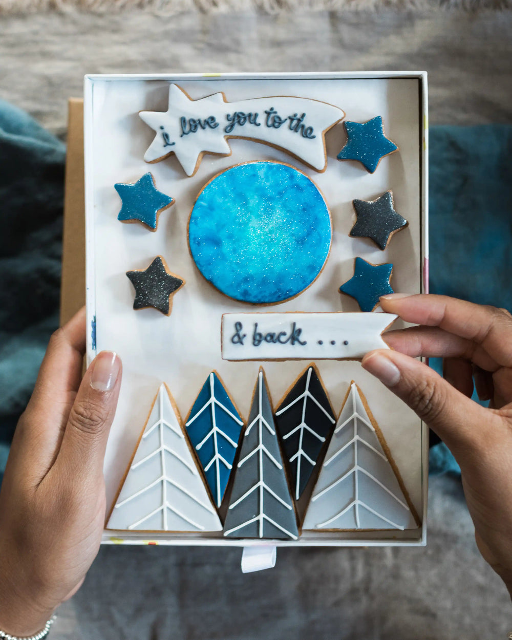 Honeywell Bakes Large I Love You To The Moon And Back Biscuit Gift Set - Biscuit set with decorative elements like stars, moon, and trees held by hands.