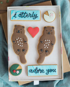 Honeywell Bakes Large Otterly Adore You Biscuit Gift Set - Decorative box with animal-shaped cookies and text 'i otterly adore you' on a textured surface.