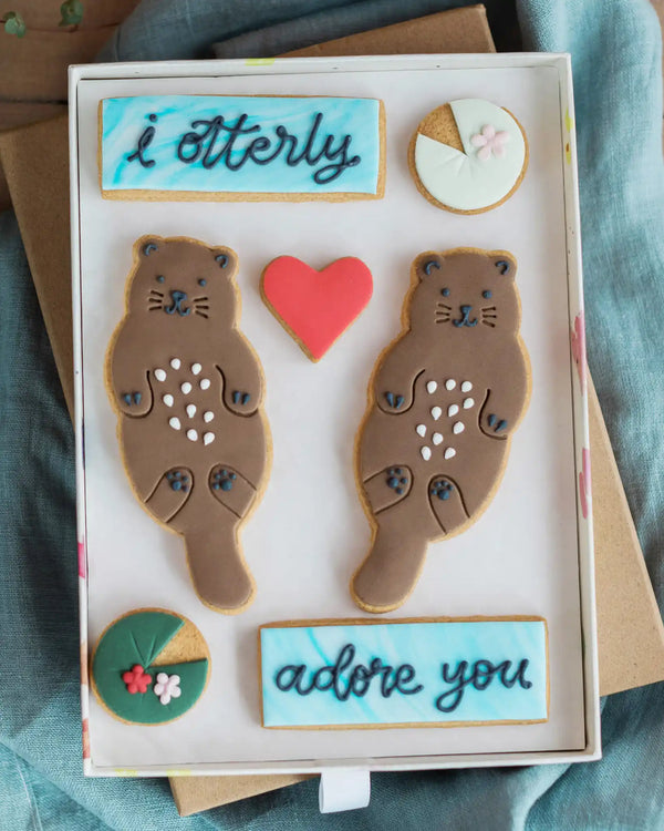 Honeywell Bakes Large Otterly Adore You Biscuit Gift Set - Decorative box with animal-shaped cookies and text 'i otterly adore you' on a textured surface.