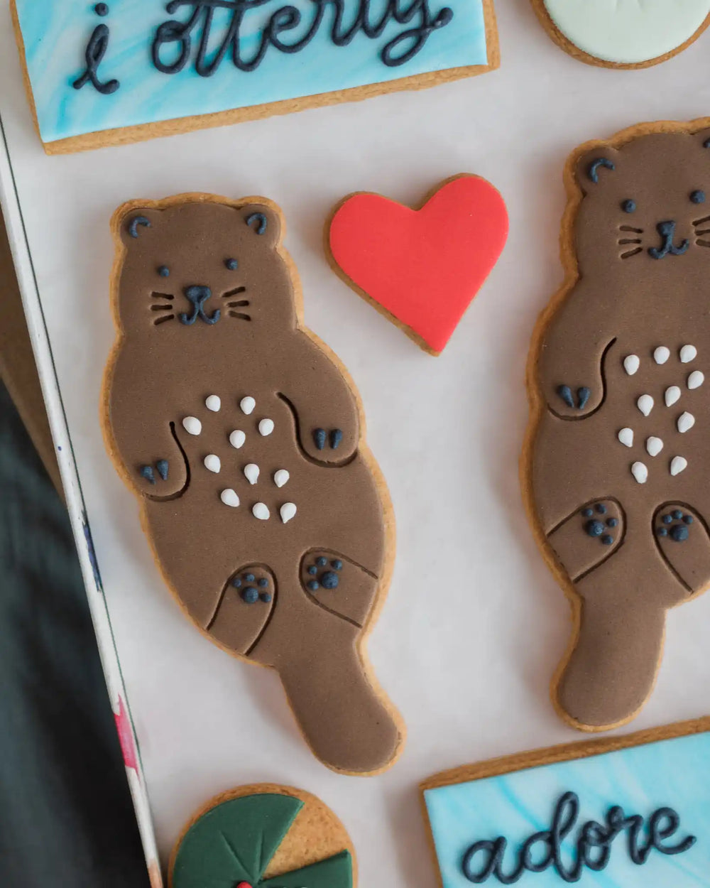 Honeywell Bakes Large Otterly Adore You Biscuit Gift Set - Decorative box with animal-shaped cookies and text 'i otterly adore you' on a textured surface.
