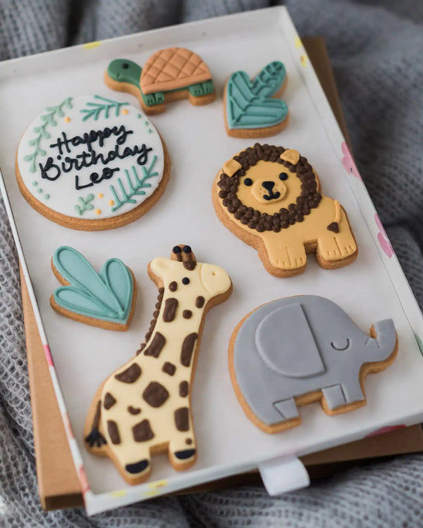 Honeywell Bakes Large Personalised Safari Biscuit Gift - Set of animal-shaped cookies including a lion, giraffe, elephant, and turtle on a white tray.