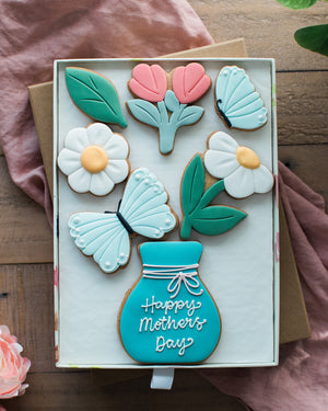 Honeywell Bakes Large Spring Biscuit Blooms - Decorative cookies shaped like flowers, leaves, and a vase with 'Happy Mother's Day' text on a wooden surface.