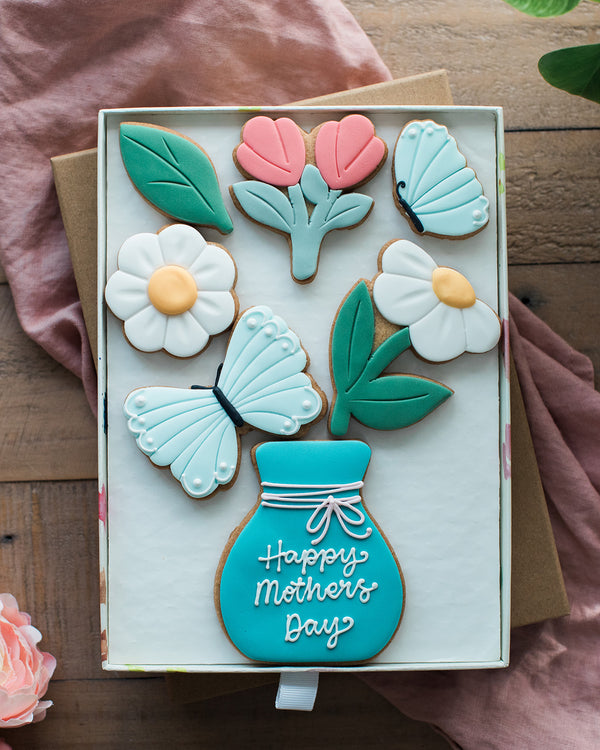 Honeywell Bakes Large Spring Biscuit Blooms - Decorative cookies shaped like flowers, leaves, and a vase with 'Happy Mother's Day' text on a wooden surface.