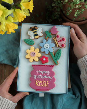 Honeywell Bakes Large Happy Biscuit Bloom Gift - Decorative birthday cookies in a box with 'Happy Birthday Rosie' text, held by hands with flowers in the background.