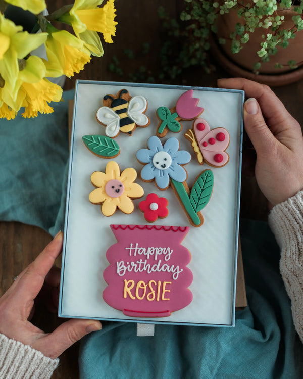 Honeywell Bakes Large Happy Biscuit Bloom Gift - Decorative birthday cookies in a box with 'Happy Birthday Rosie' text, held by hands with flowers in the background.