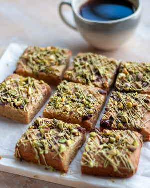 Honeywell Bakes Limited Edition Brown Butter Pistachio Blondies - squares of blondies with a pistachio and chocolate topping, on a wooden board with a cup of coffee in the background