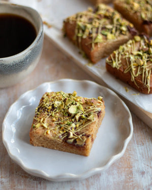 Honeywell Bakes Limited Edition Brown Butter Pistachio Blondies - squares of blondies with a pistachio and chocolate topping, on a wooden board with a cup of coffee in the background