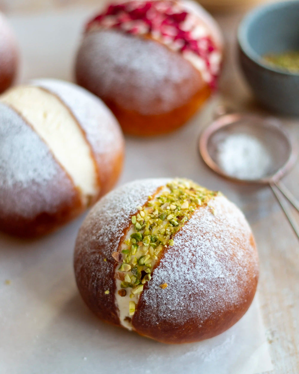 Honeywell Bakes Limited Edition Lemon & Raspberry Maritozzi Buns - large bread bun cut open and filled with cream and  lemon curd topped with pistachios and raspberries, on a wooden table with more buns in the background