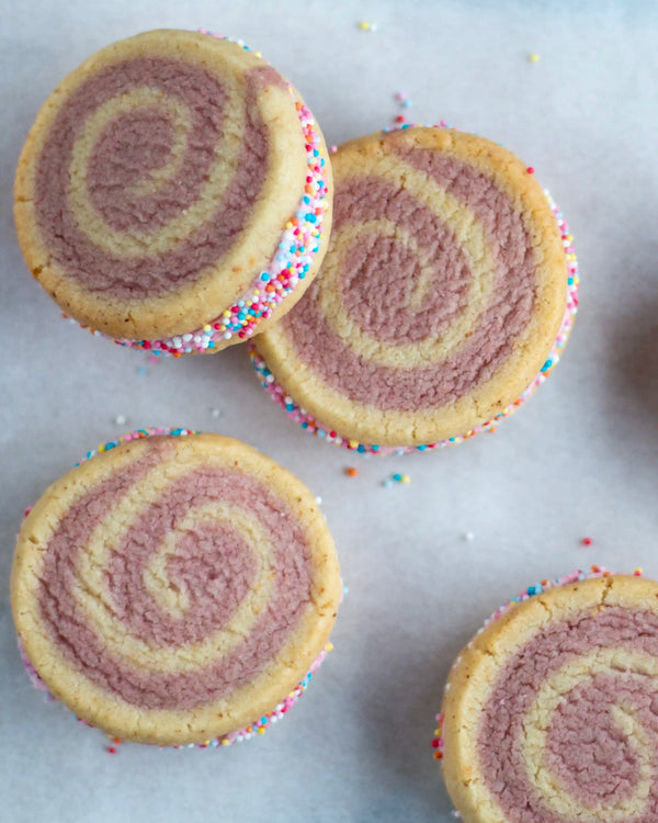 Honeywell Bakes Limited Edition Raspberry Swirl Sandwich Biscuits - rainbow swirled biscuits with a pink buttercream filling, rolled in sprinkled on greaseproof paper