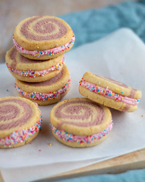 Honeywell Bakes Limited Edition Raspberry Swirl Sandwich Biscuits - rainbow swirled biscuits with a pink buttercream filling, rolled in sprinkled on greaseproof paper